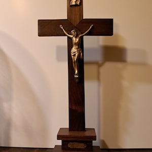 Op de afbeelding: Een houten kruisbeeld met een gouden Jezusfiguur. Het kruisbeeld heeft een voet met een klein plakkaat met de tekst "In Memory Of".
