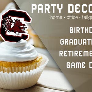 May include: A cupcake topped with white icing and a red, black and white University of South Carolina Gamecock logo. The text "PARTY DECOR" is in the background, along with the words "home - office - tailgating", "BIRTHDAY", "GRADUATION", "RETIREMENT", and "GAME DAY".