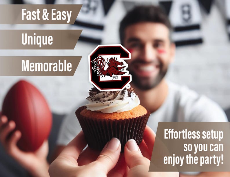 May include: A cupcake with white frosting and chocolate sprinkles topped with a red and black University of South Carolina Gamecocks logo cupcake topper. The cupcake is being held by a person's hand. The background is blurred and shows a person wearing a white shirt with a black and white striped pattern.