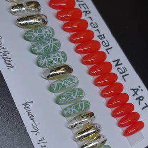 Puede incluir: Una colección de uñas postizas con varios diseños. Algunas uñas son rojas lisas, otras presentan láminas doradas y otras tienen una base verde con diseños abstractos blancos. El texto "WER-r-bəl NÄL ÄRT" es visible.