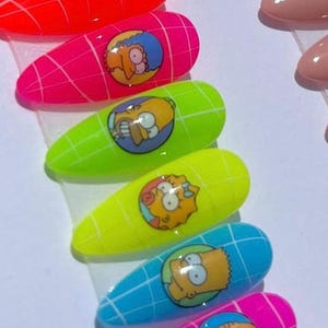 Puede incluir: Un conjunto de uñas artificiales largas en forma de almendra, de colores vibrantes. Cada uña presenta un diseño de personaje de dibujos animados sobre un fondo de cuadrícula. Los colores incluyen rojo, rosa, verde, amarillo, azul y rosa. El personaje es Homer Simpson.