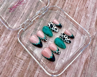 May include: A set of ten almond-shaped press-on nails in a clear plastic case. The designs include a nude base with black tips and teal dots, solid teal marble patterns, and black and white cow print patterns. The case lid features a logo.