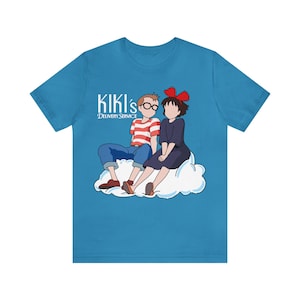 May include: A turquoise blue t-shirt with a graphic of Kiki and Tombo from the movie Kiki's Delivery Service. The text "Kiki's Delivery Service" is printed below the graphic.