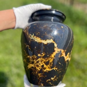 Könnte beinhalten: Eine weiße Keramik-Tasse mit schwarzem Henkel und dem Text "But First, Coffee" in schwarzer, handschriftlicher Schrift. Die Tasse steht auf einer weißen Oberfläche.