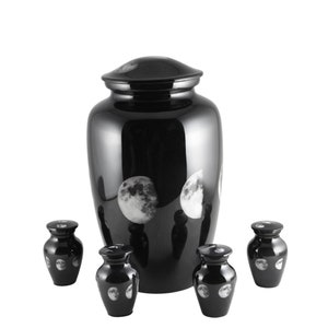 May include: A set of five black urns with a moon phase design. The largest urn is taller than the four smaller urns. The urns are made of metal and have a shiny finish.