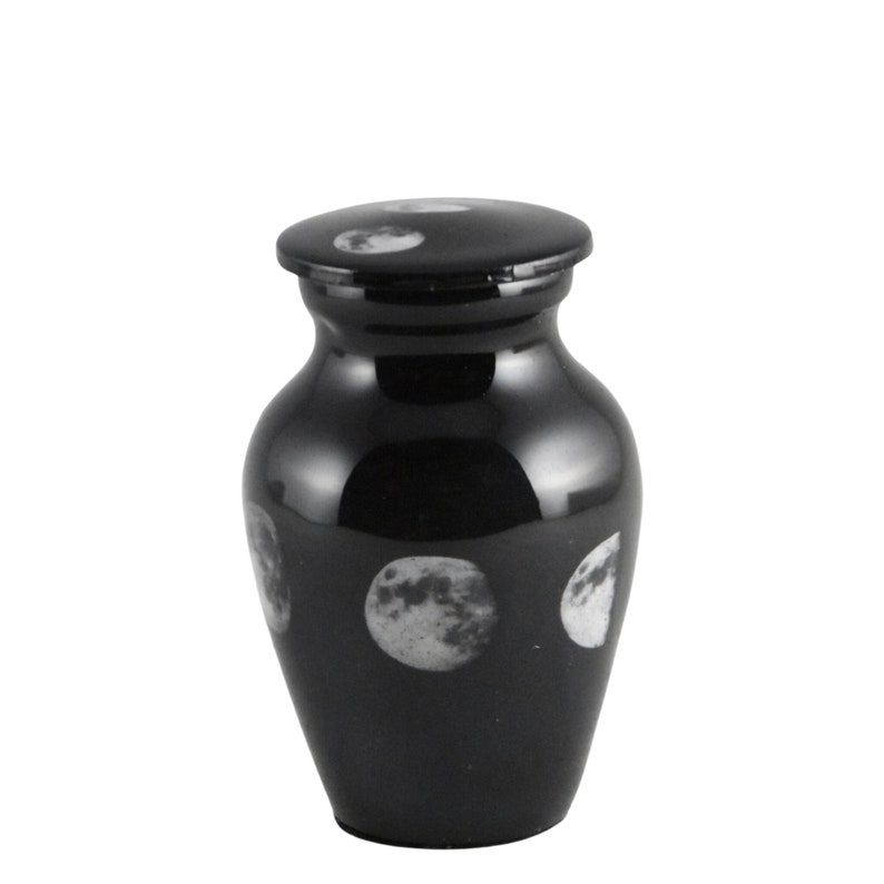 May include: Black cremation urn with a moon phases design. The urn has a lid and is made of metal.