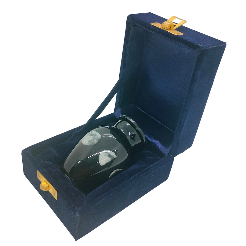 May include: Black cremation urn with a moon and star design, in a blue velvet box with a gold latch.