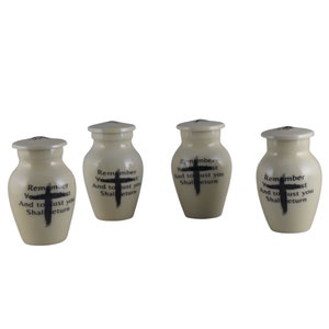 May include: Four small white ceramic urns with black cross designs and the text "Remember You are dust And to dust you Shall return" on each.
