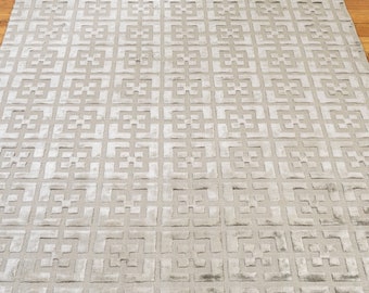 May include: A light gray area rug with a geometric pattern. The pattern is made up of squares and rectangles, and it is embossed into the rug.