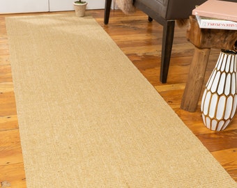 May include: A natural fiber runner rug in a light beige color. The rug is woven with a subtle texture and has a rectangular shape. It is placed on a wooden floor in a home setting.