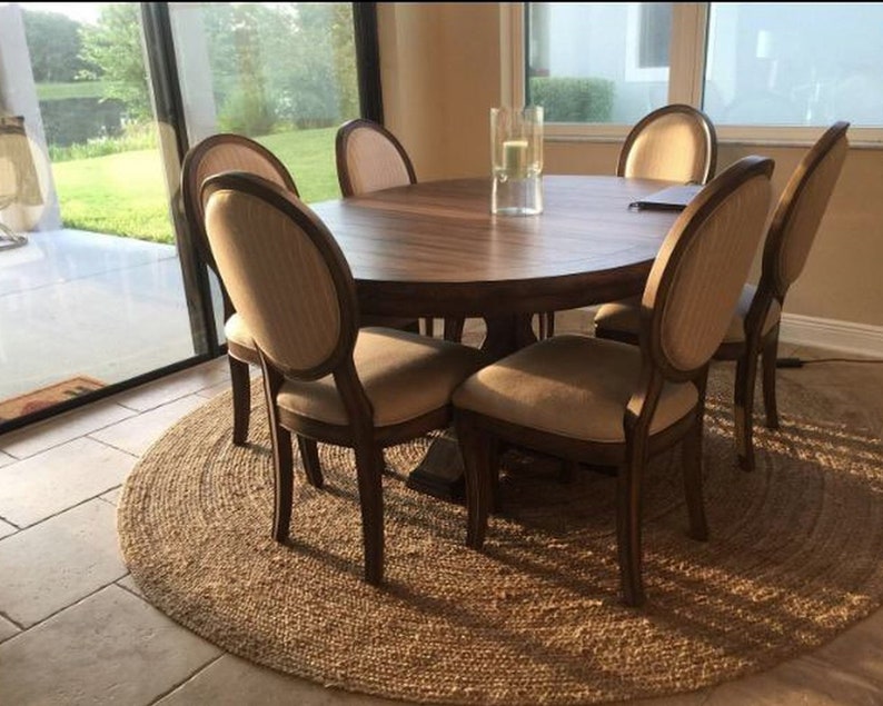 May include: A round wooden dining table with six chairs. The table has a natural wood finish and the chairs are upholstered in a light beige fabric. The table is set on a natural fiber rug.
