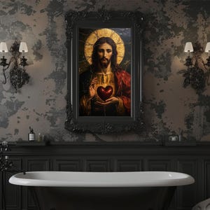 K&ouml;nnte beinhalten: Ein gerahmtes Gem&auml;lde von Jesus Christus mit einem goldenen Heiligenschein und einem roten Gewand, der ein rotes Herz in seinen H&auml;nden h&auml;lt. Das Gem&auml;lde ist vor einer dunklen, strukturierten Wand mit einer schwarzen Badewanne im Vordergrund platziert.