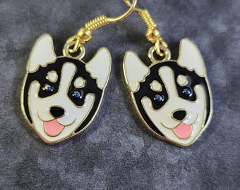 May include: A pair of gold dangle earrings featuring a black and white husky dog design with blue eyes and a pink tongue.