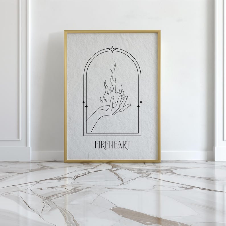 May include: A black and white line art print of a hand holding a flame with the word "FIREHEART" below it. The print is framed in a gold frame and is hanging on a white wall.