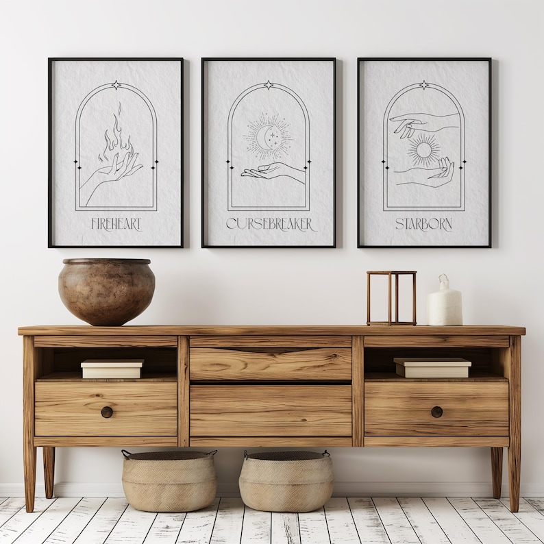 May include: Three black framed prints with white backgrounds and black line drawings of hands holding a flame, a crescent moon, and a sun. The prints are titled "Fireheart", "Cursebreaker", and "Starborn".