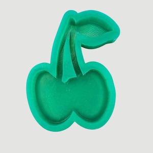 May include: A green cherry-shaped cookie cutter. The cutter is made of plastic and has a detailed design, including the stem and leaf. The cherry shape is a classic design for baking and crafting projects.