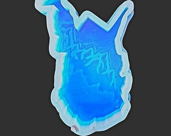 May include: A blue and white abstract resin pendant with a unique shape. The pendant has a layered effect, with shades of blue and white creating depth. The edges are outlined in white, and the background is black.