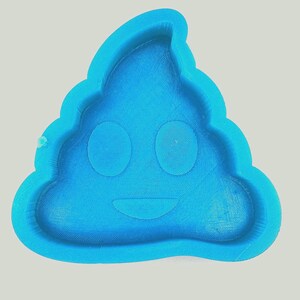 May include: A bright blue silicone mold in the shape of a smiling poop emoji. The mold has two circular eye indentations and a curved mouth. The edges of the mold are rounded.