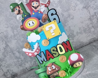 May include: A two-tiered birthday cake decorated with a Super Mario Bros. theme. The cake is blue and green with a question mark block, coins, and a pipe. The top tier features a red and blue Mario figure, a green Luigi figure, and a red mushroom. The bottom tier features a green Koopa Troopa figure and the name "MASON" in red, yellow, and blue letters.