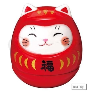 May include: A red Daruma doll with a white cat face, featuring black eyes, whiskers, and a pink nose. The doll has gold accents and the Japanese character for "fortune" on the front. The doll has a rounded shape and cat ears.