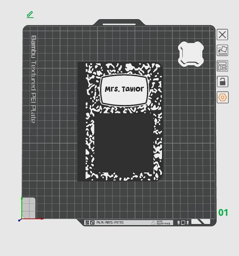 May include: A black and white composition notebook with the name "Mrs. Taylor" in a white label. The notebook is on a textured gray surface with a grid pattern. The image also shows a white object and some technical details.