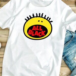 May include: White t-shirt with a yellow and black graphic of a cartoon face with the text "ALL BLACK" in red.