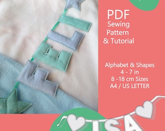May include: A soft, light blue and white fabric background with a garland spelling "ISA" and a banner with the text "PDF Sewing Pattern & Tutorial". The image also features felt letters and stars in shades of blue and green.