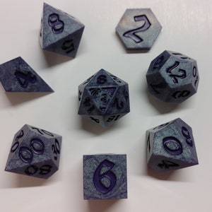 May include: A set of eight grey and purple dice with various numbers and symbols. The dice are made of a textured material and have a speckled appearance.