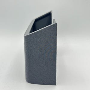 May include: A dark gray, U-shaped wall-mounted holder with a textured, matte finish. The object features a rectangular front panel, two side walls, and an open top, designed with a clean, geometric structure and a solid, uniform appearance.