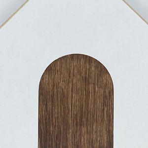 May include: White wooden house with a brown wooden door. The house is a simple design with a rounded archway for the door.