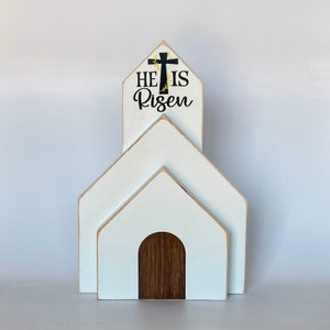 May include: White wooden church-shaped tiered decor with a black cross and the text "He is Risen" on the top tier.