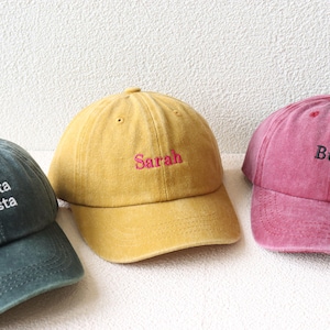 May include: Three different colored baseball caps with embroidered text. The first cap is green with white text that reads "eat pasta run fasta". The second cap is yellow with pink text that reads "Sarah". The third cap is pink with black text that reads "BUNDLE".