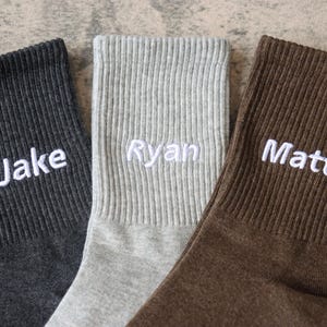 Peut inclure: Trois paires de chaussettes en tissu de couleurs différentes avec des noms brodés en blanc : Jake, Ryan et Matt.