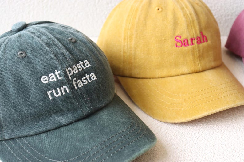 May include: Two baseball caps, one green with the text "eat pasta run fasta" embroidered in white, and one yellow with the name "Sarah" embroidered in pink.
