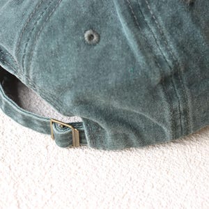 May include: A dark green cotton baseball cap with a brass buckle closure.