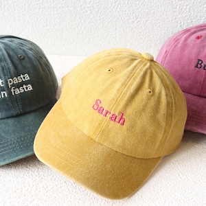 May include: Three different colored baseball caps with embroidered text. The first cap is dark green with white text that says "eat pasta run fasta". The second cap is yellow with pink text that says "Sarah". The third cap is pink with black text that says "Bundle".