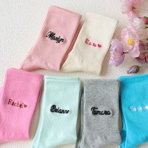 Könnte beinhalten: Sechs Paar bunte Socken mit gestickten Namen, darunter "Rachel", "Elaine", "Marilyn", "Tamara", "Brianne" und "Sarah".
