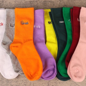 Könnte beinhalten: Zehn Paar bunte Socken mit gestickten Namen, darunter "Nock", "Sarah", "Ashley", "Shawn", "Danny", "Larry", "Jenny", "Tommy", "Lucy" und "Sammy".