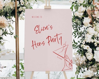Könnte beinhalten: Ein rechteckiges, hellrosa Willkommensschild auf einer Holzstaffelei mit rotem Text, der Welcome to Eliza's Hens Party lautet. Das Schild enthält eine rote Strichzeichnung eines Martiniglases mit einer Kirsche und dem Hashtag #ELIZASHENS.