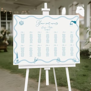 May include: A white wedding seating chart on an easel with a light blue wavy border and decorative illustrations. The text "Your seat awaits" is displayed, along with the names Emily & Nathan and the date.