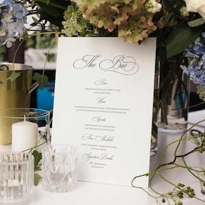 May include: A white menu with the title "The Bar" in a decorative script font. The menu lists drinks including beer, wine, spirits, non-alcoholic beverages, and signature drinks.