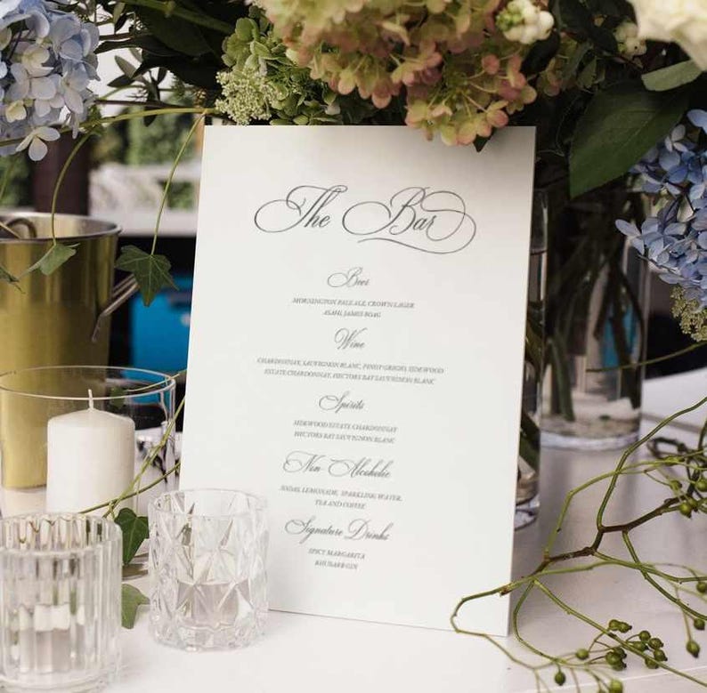 May include: A white menu with the title "The Bar" in a decorative script font. The menu lists drinks including beer, wine, spirits, non-alcoholic beverages, and signature drinks.