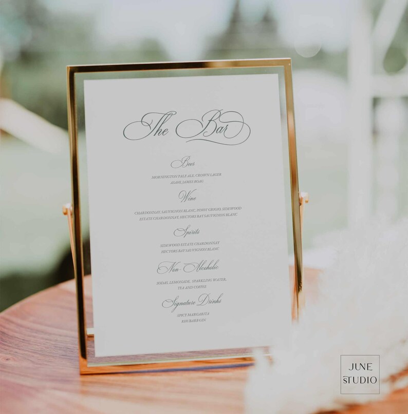 May include: A gold-framed sign with a white background and black text lists the bar menu for a wedding. The menu includes beer, wine, spirits, non-alcoholic drinks, and signature drinks.