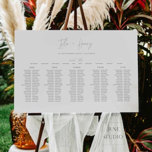 Può includere: Un cartello rettangolare per il tableau de mariage con sfondo grigio chiaro e testo nero. Riporta i nomi Isla + Harvey, la data 16 settembre 2023, la località Victoria e un elenco di invitati organizzato per numeri di tavolo da uno a cinque.