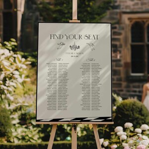 May include: A white wedding seating chart with black text. The chart is titled "Find Your Seat" and lists the names of guests assigned to each table. The chart also includes the couple's names, "Tyler & Simon", and the wedding date, "26.11.0X".