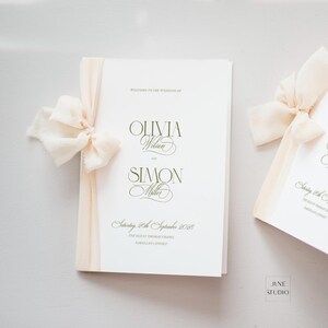 以下が含まれることがあります： Welcome to the wedding of Olivia Wilson and Simon Miller, Saturday, 28th September 2028, The Old St Thomas Chapel, Narellan, Sydneyと書かれたダークグリーンの文字と、クリーム色のシフォンリボンがあしらわれた白い結婚式プログラムの小冊子。