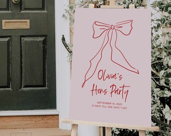 Puede incluir: Un letrero rectangular sobre un caballete de madera con fondo malva claro y una ilustración de lazo en línea roja. El texto dice: Olivia's Hens Party, SEPTEMBER 16, 2025, 21 DAYS TILL SHE SAYS "I DO". El letrero se muestra en un entorno exterior.