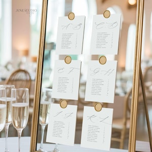 May include: A gold framed mirror displays six seating arrangement cards for a wedding. Each card is held by a gold wax seal. The cards have elegant calligraphy with names and table numbers. The mirror reflects a blurred background.