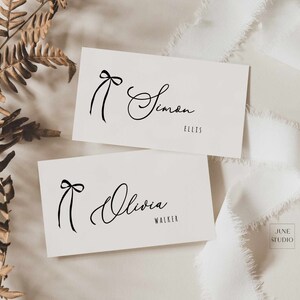 May include: Two white cards with black calligraphy names and a simple black bow design. The top card reads "Simon Ellis" and the bottom card reads "Olivia Walker".