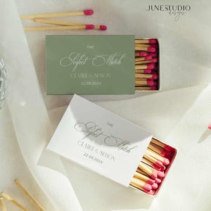 May include: Two matchboxes, one sage green and one white, with the text "The Perfect Match" and names. The matches have pink tips. The date 22.09.202X is also printed on the boxes. The image is on a white background.
